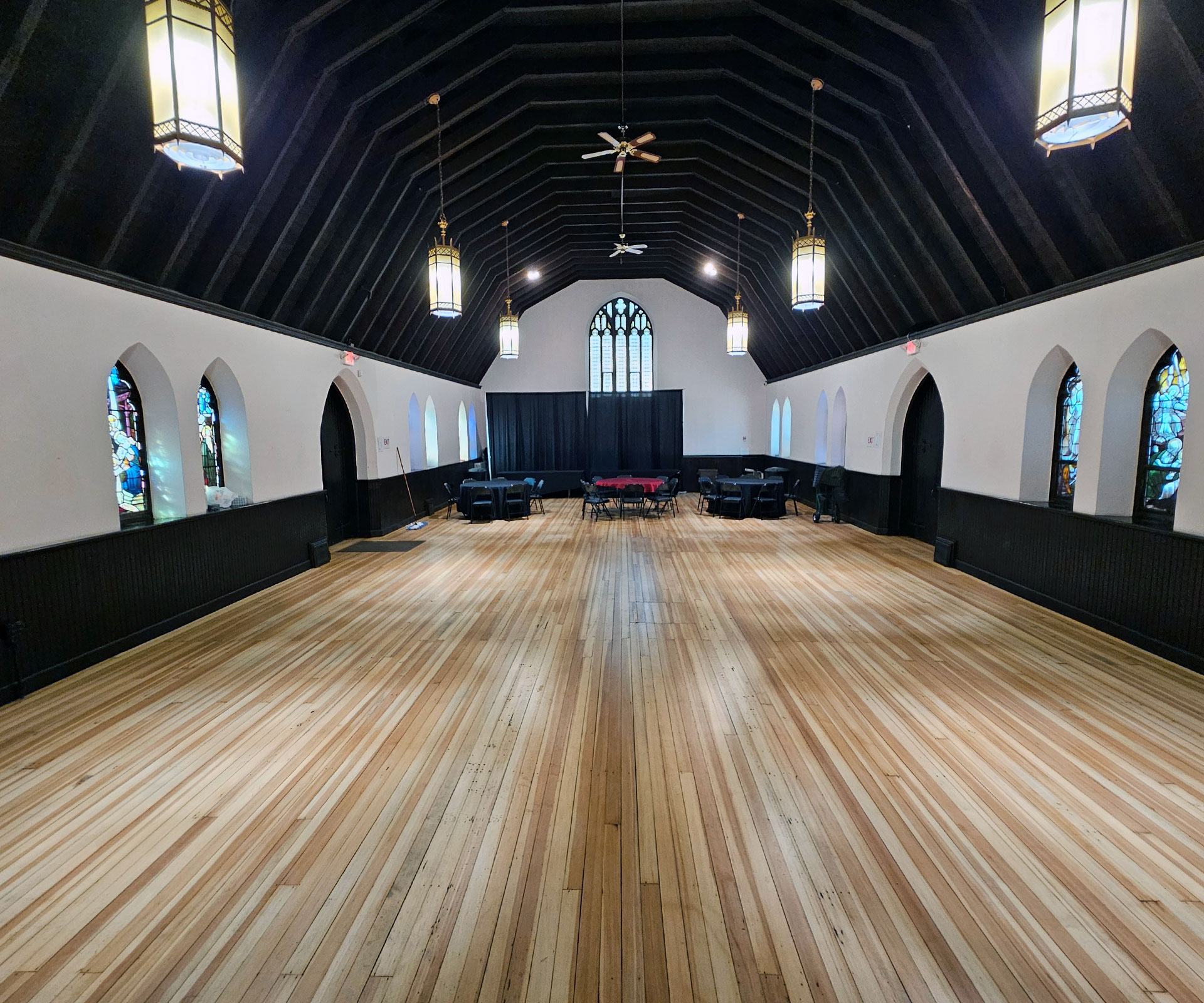 The hall empty and ready — hardwood floors stretching the full length beneath a dramatic vaulted ceiling with stained glass windows lining both sides.